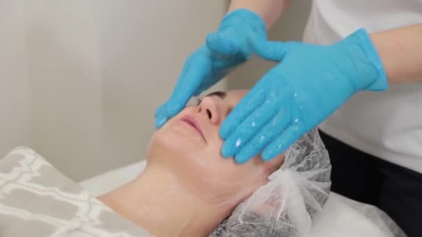 Vrouw schoonheidsspecialiste massages het gezicht van een klant. — Stockvideo