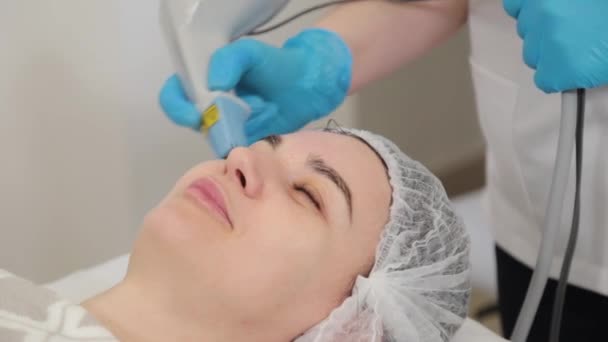 Mulher cosmetologista trata clientes rosto com laser. — Vídeo de Stock