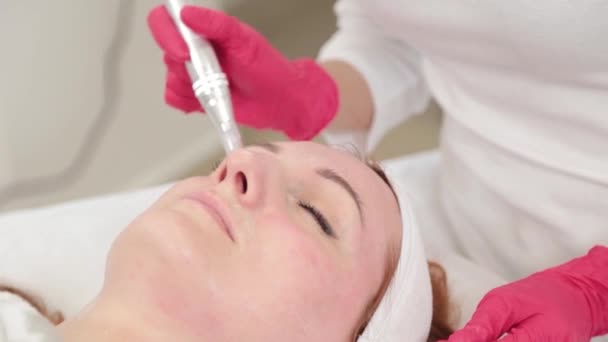 Kvinnlig kosmetolog behandlar sitt ansikte med en apparat på kosmetologikontoret. — Stockvideo