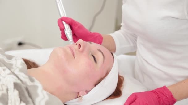 Femme cosmétologue traite son visage avec un dispositif dans le bureau de cosmétologie. — Video