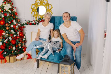 Güzel, genç, mutlu bir aile yeni yıl ağacının yanındaki koltukta..