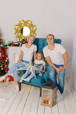 Güzel, genç, mutlu bir aile yeni yıl ağacının yanındaki koltukta..