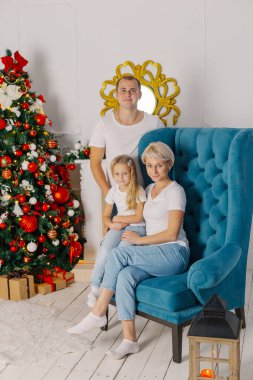 Güzel, genç, mutlu bir aile yeni yıl ağacının yanındaki koltukta..
