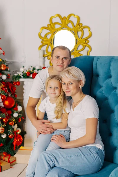 Belle jeune famille heureuse et joyeuse sur un fauteuil près de l'arbre du Nouvel An. — Photo