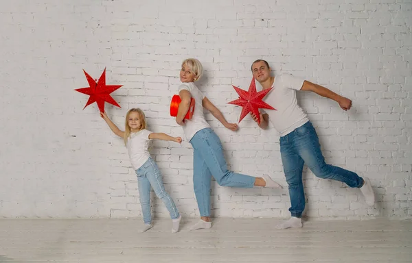 Bela família jovem feliz perto da parede com estrelas de Natal. Fotos De Bancos De Imagens