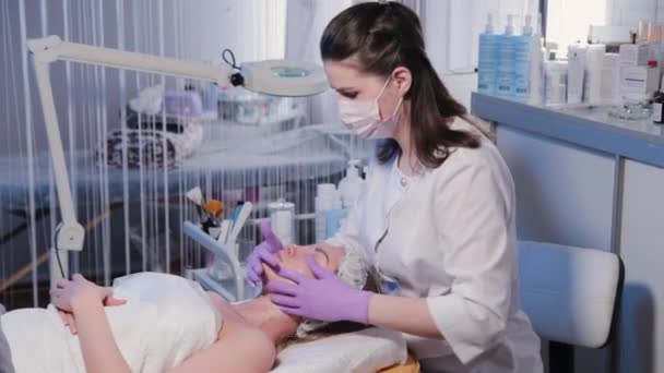 Женщина косметолог наносит крем на лицо женщины. — стоковое видео