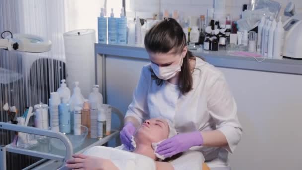 Woman beautician washes off cream from womans face with wet wipes. — Stock Video