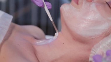 Kadın güzellik uzmanı yüzüne fırçayla krem sürüyor.