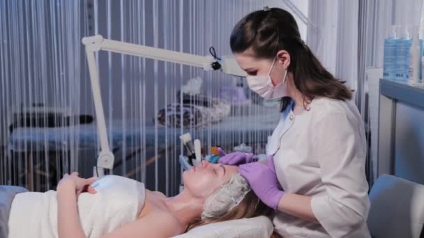 Kobieta kosmetyczka masuje krem na twarz kobiet. — Wideo stockowe