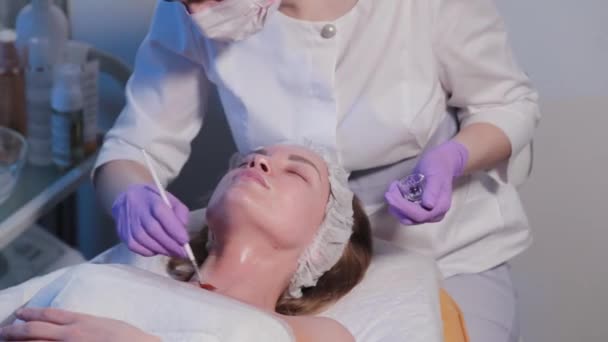 Mujer esteticista aplica suero con cepillo a cara de mujer. — Vídeos de Stock