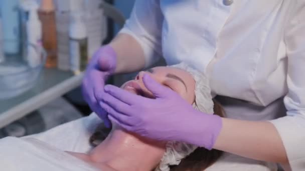 Женщина-косметолог намазывает кремом лицо женщины. — стоковое видео