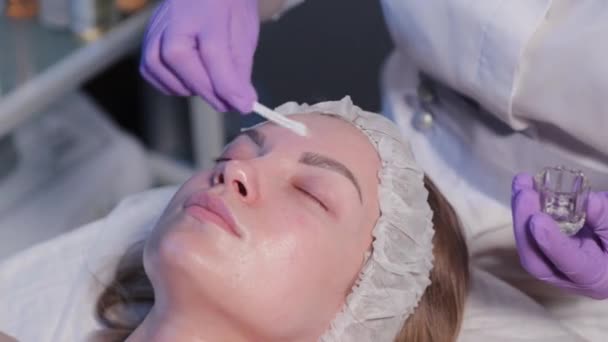 Femme esthéticienne applique liquide sur les femmes visage avec coton-tige. — Video