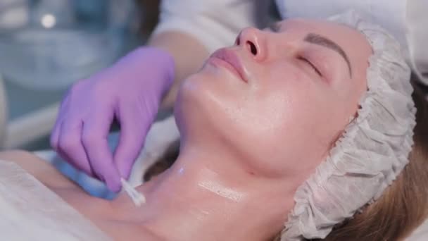 Žena kosmetička aplikuje tekutinu na ženskou tvář s bavlněnými tampony. — Stock video