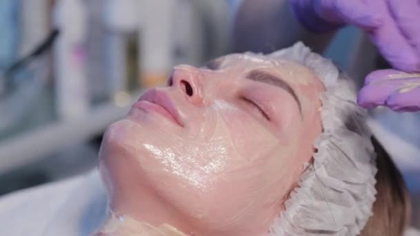 Kobieta kosmetyczka nakłada krem na kobietę na twarz specjalną szczotką. — Wideo stockowe