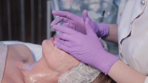 Kobieta kosmetyczka nakłada krem na kobietę na twarz specjalną szczotką. — Wideo stockowe