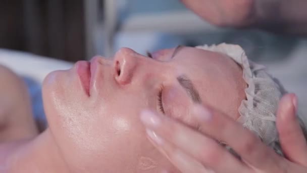 Vrouw cosmetoloog brengt cosmetische crème op vrouw gezicht. — Stockvideo