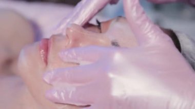 Kadın güzellik uzmanı kadın yüzüne krem sürüyor..
