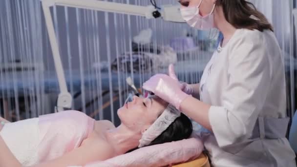 Kobieta kosmetyczka stosuje krem do twarzy kobiety. — Wideo stockowe