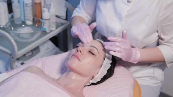 Kvinna kosmetolog applicerar grädde på kvinnans ansikte. — Stockvideo
