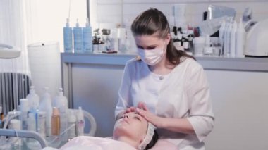 Kadın güzellik uzmanı kadın yüzüne krem sürüyor..