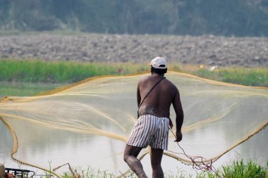 Balık adam ağıyla küçük bir gölde balık tutuyor, Yamuna Nehri yakınlarında, Delhi, Hindistan Ekim 2017