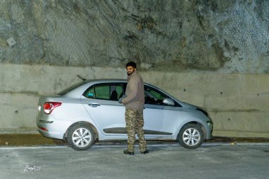 Beyaz gömlekli ve siyah ceketli genç adam şehirde yolda duruyor.