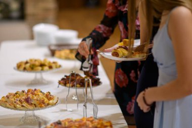Konuklar, şenlikli bir toplantı ya da özel bir kutlama sırasında çeşitli parti yiyecekleri ve parmak yiyecekleriyle bezenmiş bir büfeden hamur işine sarılmış lezzetli mezeler ve mini sosisliler seçiyorlar.
