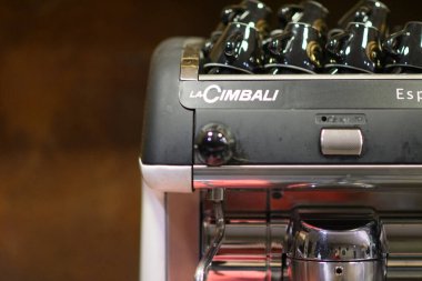 Milan, İtalya - 1 Temmuz 2025 Kahve sevenler ve baristalar için arka planda demleme ekipmanları ve fincanları gösteren bir kafede profesyonel bir espresso makinesini kapatın