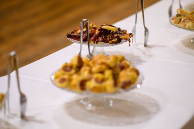 Beyaz masa örtüsü üzerinde sanatsal olarak düzenlenmiş çeşitli tuzlu ve tatlı ısırıkların yer aldığı resmi bir etkinlikte ya da büfede servis edilen lezzetli bir aperatif ve tatlı yayılımı.