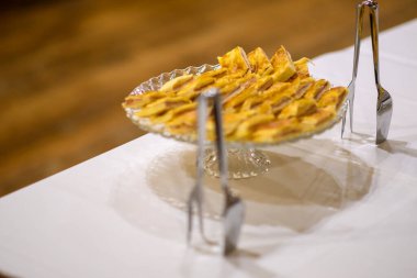 Delicious Homemade Apple Tart Baked Golden Brown Served Freshly Cut on a Clear Glass Cake Stand Ready for Guests to Enjoy at a Festive Gathering