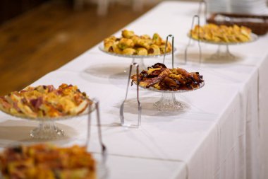 An Elegant Wedding Buffet Presentation Featuring Delicious Appetizers and Savory Dishes Served on a White Tablecloth Displayed on Crystal Pedestals for Guests at an Event