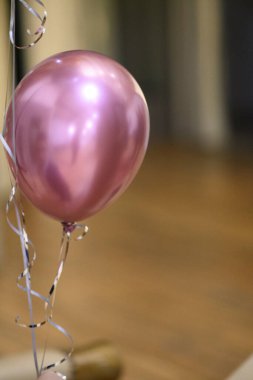 A Single Shiny Rose Gold Balloon with Silver Ribbons Floats Upwards Against a Blurred Golden Background Symbolizing Celebration and Joyful Occasion Moments