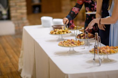 Özel bir etkinlik ya da kutlama yemeği partisi için uzun bir masa örtüsüne yerleştirilmiş çeşitli aperatifler ve lezzetli küçük lokmalarla servis edilen zarif bir açık büfe.