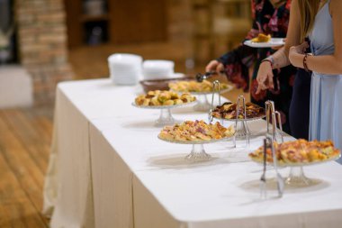 Katlı tabaklar ve dekoratif tezgahlarda sunulan çeşitli lezzetli aperatifler ve parmak yiyeceklerin yer aldığı zarif bir açık büfe masası.