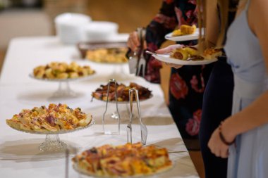 Bir partide ya da bir etkinlikte kendilerine çeşitli lezzetli yiyecek ve tatlılarla dolu bir büfe masasında servis yapan insanlar.