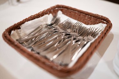 A Rustic Woven Basket Filled with Gleaming Silver Forks Lined with Crisp White Napkins on a Table Setting Ready for Dining