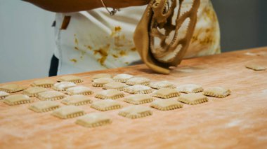 Usta fırıncı, profesyonel bir mutfakta, ahşap bir masanın üzerine un serpiştirilmiş küçük hamur kareleri hazırlıyor.