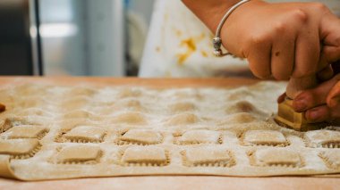 Becerikli eller, mutfak atmosferinde bir şaheser yaratmak için kare kesiciyle bastırarak taze makarna kareleri ustalıkla hazırlıyorlar.