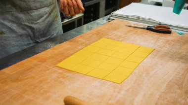 Şef lezzetli bir yemek için ahşap bir masada hamuru küçük kareler halinde keserek taze makarna hazırlıyor.