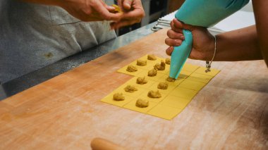 Zanaatkar elleri, ahşap bir yüzey üzerinde boru torbası kullanarak hassas makarna hamuru ve ev yapımı İtalyan geleneğini titizlikle hazırlar.