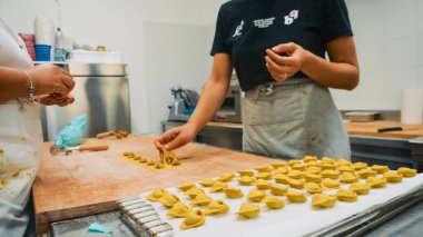 Piacenza, İtalya - 1 Ekim 2025 Taze ahşap bir yüzey üzerinde ev yapımı makarnayı titizlikle hazırlayan becerikli eller açık ve temiz bir profesyonel mutfak ortamında mutfak sanatını sergiliyor ve