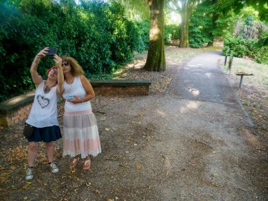 Güneşli bir günde parkta selfie çeken iki kadın dışarıda eğleniyor ve sosyal medyada bir an paylaşıyorlar.