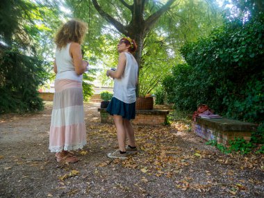 Güneşli bir günde, arka planda ağaçlar ve yapraklarla parkta sohbet eden iki kadın yaz mevsimi boyunca.