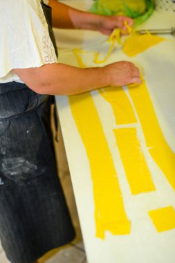 Geleneksel İtalyan mutfak becerilerini gösteren bir bıçakla ev yapımı makarna hamurunu beyaz ahşap bir masada uzun sarı bantlara ustalıkla kesen birinin genel bakış açısını kapatın.