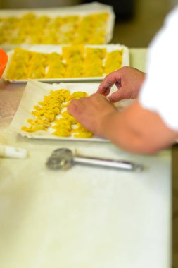 Becerikli ellerin, mutfak düzeninde yemek hazırlama işlemi sırasında beyaz tepside yeni yapılmış hamur hamuru şekillerini dikkatlice düzenlemesi.