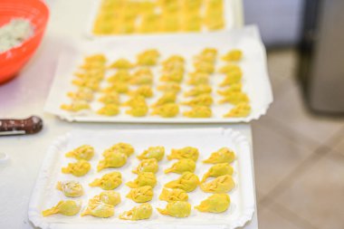 Mutfak ortamında pişirmeye ve pişirmeye hazır tepsilere konmuş küçük doldurulmuş hamur köftelerine dönüştürülmüş ev yapımı taze hazır makarna.