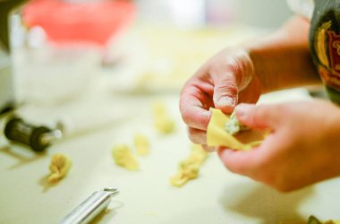 Eller titizlikle katlanmış taze makarna hamuru ev yapımı İtalyan yemeği deneyimi için peynir ve otlarla dolu hassas tortellini oluşturuyor.