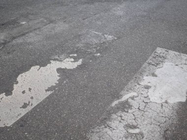Asfalt bir yolda yıpranmış ve çatlamış boyalı bir yaya geçidine yakın görüş, bakım ve onarım ihtiyacını vurguluyor