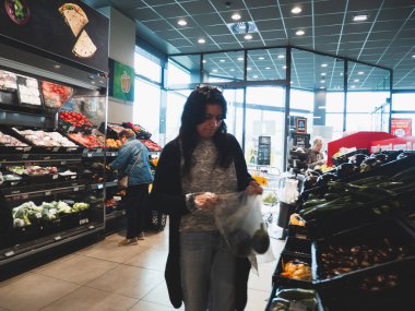 Lombardy, İtalya - 1 Ekim 2025 Kadın yoğun bir İtalyan süpermarketinde canlı bir üründen taze avokado seçiyor.