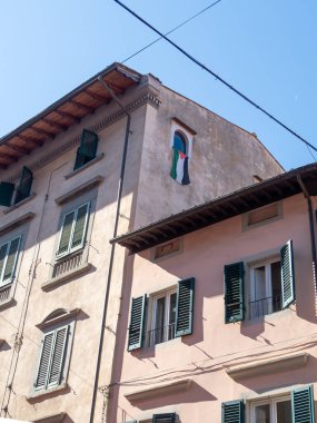 Pisa, İtalya - 16 Ekim 2025 Filistin bayrağı renklerini sergiliyor, yıpranmış bir duvarda klasik kemerli bir pencereden sarkıyor, dayanışmayı temsil ediyor